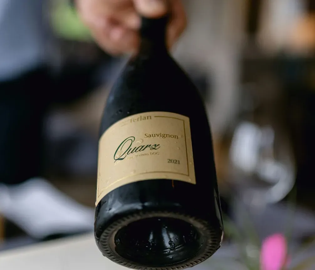 Hand holding a bottle of Sauvignon Quarz wine, labeled 2021, with a blurred indoor background.