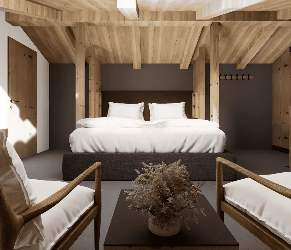 A cozy hotel room in Alta Badia featuring a wooden ceiling and walls, a large bed with white linens, two armchairs with cushions, and a small table with a flower arrangement.