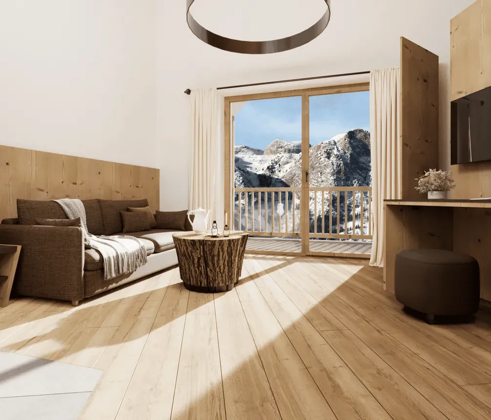 A cozy hotel room with wooden accents, a large window showing snowy mountains, a brown sofa with cushions, a small wooden coffee table, and a wall-mounted TV.