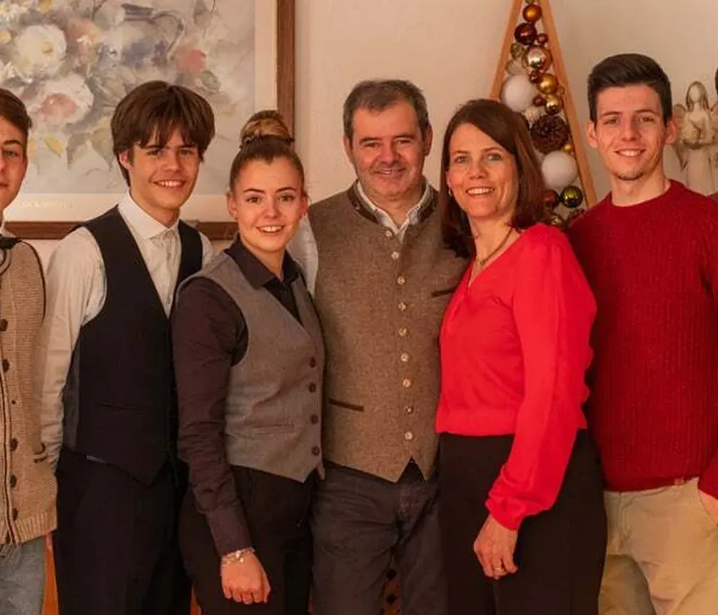 Familie und Freunde stehen zusammen im Innenraum, lachend und lächelnd, bei einer Feier, vor einer weihnachtlich dekorierten Wand im Hotel La Müda in Alta Badia.