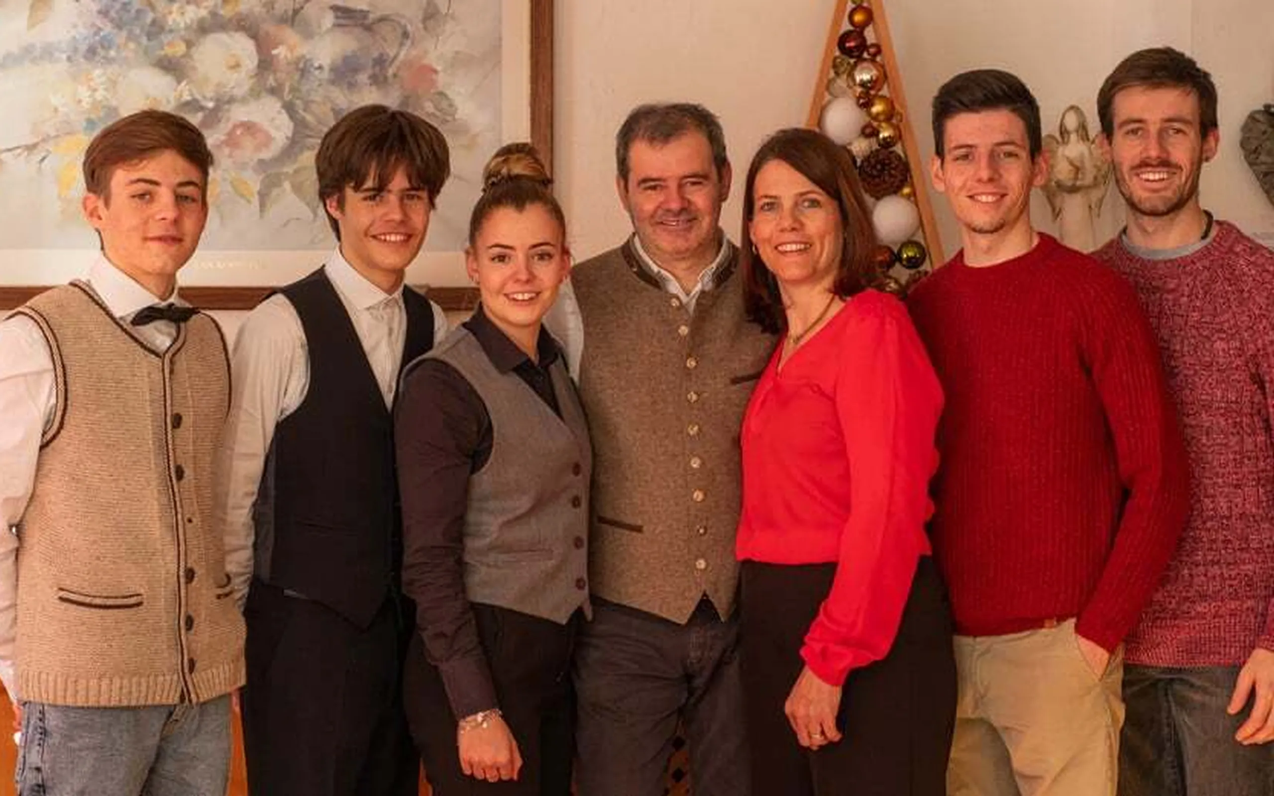 Familie und Freunde stehen zusammen im Innenraum, lachend und lächelnd, bei einer Feier, vor einer weihnachtlich dekorierten Wand im Hotel La Müda in Alta Badia.