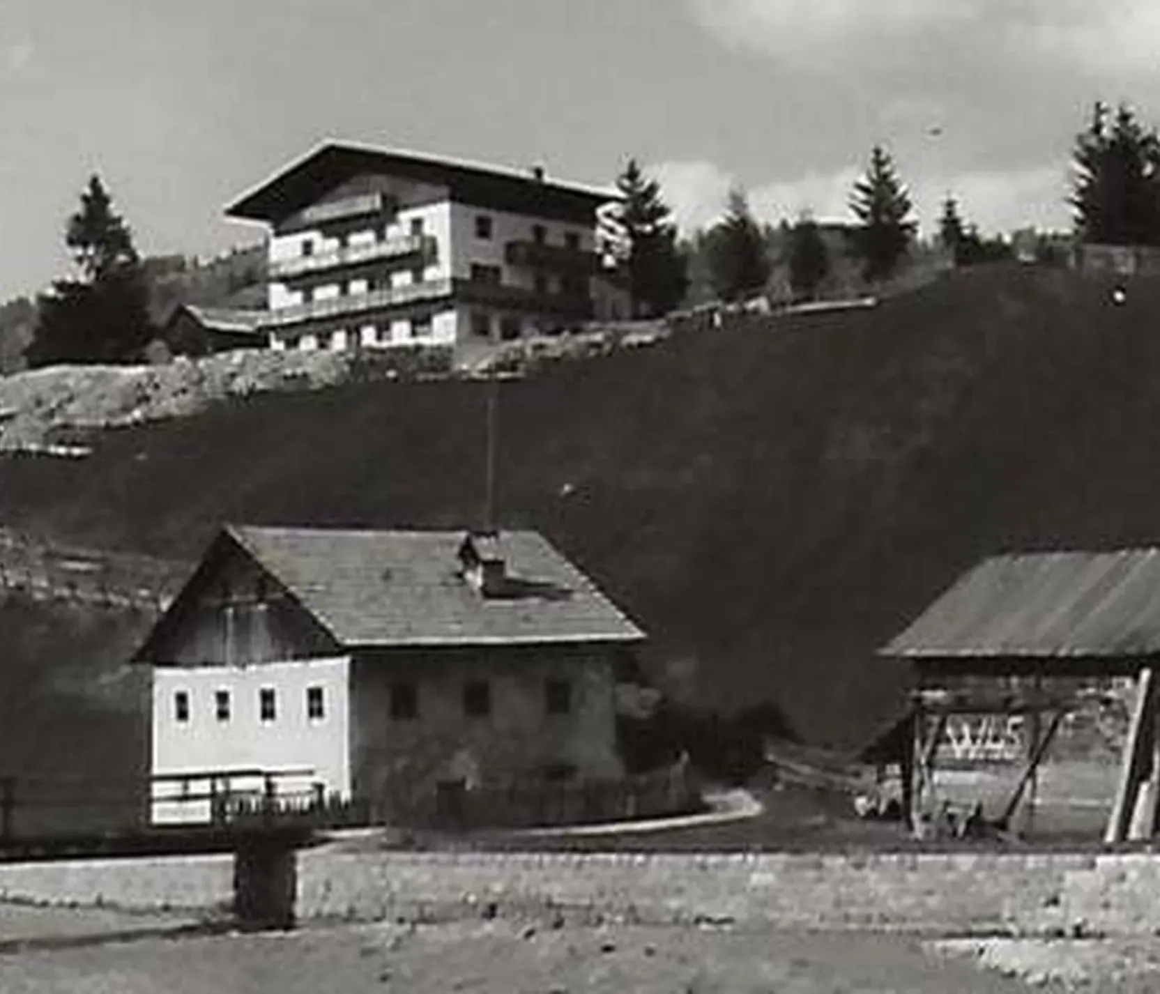 Dorf mit traditionellen Holzhütten und modernem Hotel im Hintergrund in Alta Badia, Dolomiten, unter bewölktem Himmel.