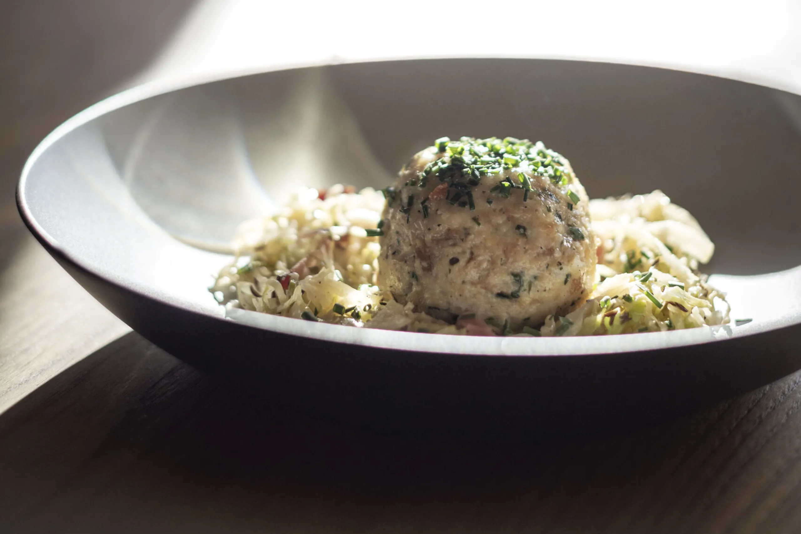Pallina di pesce con insalata di cavolo cappuccio e vino bianco in un bicchiere, in cucina con luce naturale.