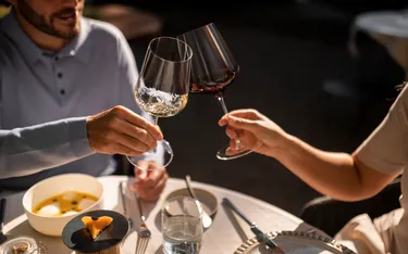 Due persone brindano con vino in un ristorante, con piatti e bicchieri eleganti sul tavolo, atmosfera intima e illuminazione calda.