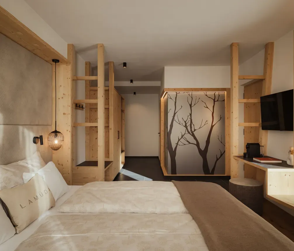 Modern hotel room with wooden accents, featuring a cozy bed, soft beige linens, decorative hanging lamp, and a tree silhouette wall design. Peaceful ambiance.