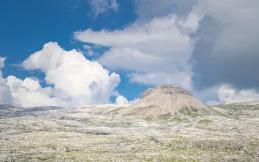 A rocky mountain formation with slopes covered in grass and rock, under a partly cloudy sky in the Dolomites, Alta Badia region.
