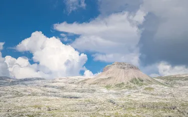 A rocky mountain formation with slopes covered in grass and rock, under a partly cloudy sky in the Dolomites, Alta Badia region.