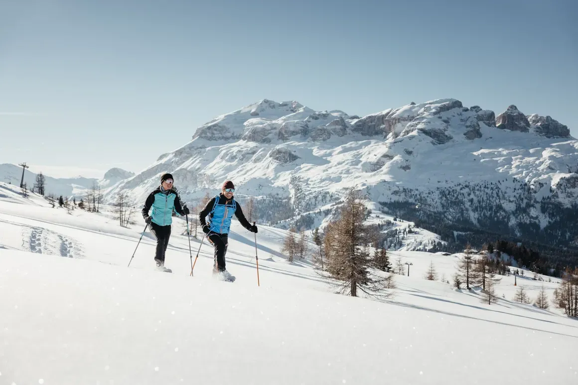 Due sciatori che salgono sulla neve con lo sfondo le montagne innevate delle Dolomiti.