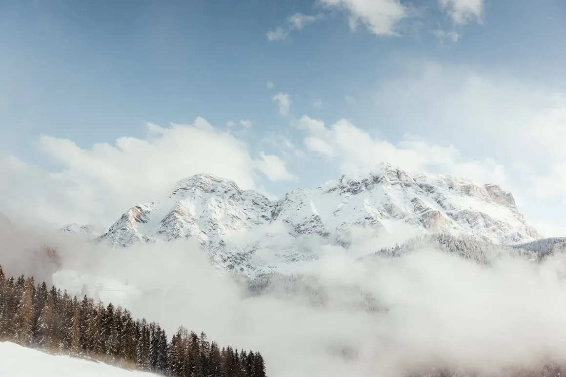 Montagne innevate con nuvole e cielo sereno sopra una foresta di pini in Dolomiti, Alta Badia.
